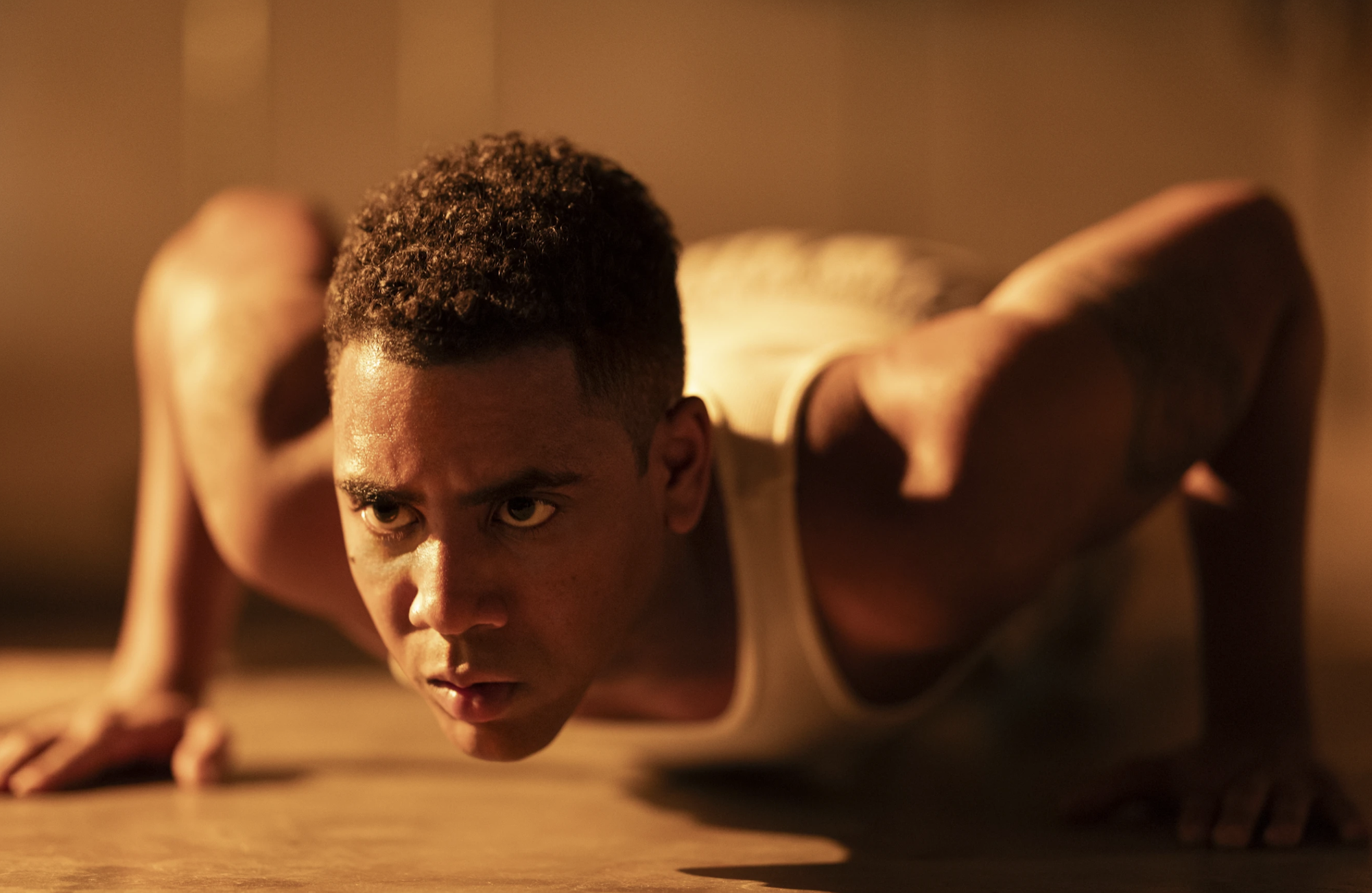 A Black man in deep concentration lies flat on his stomach getting ready to do a push up.