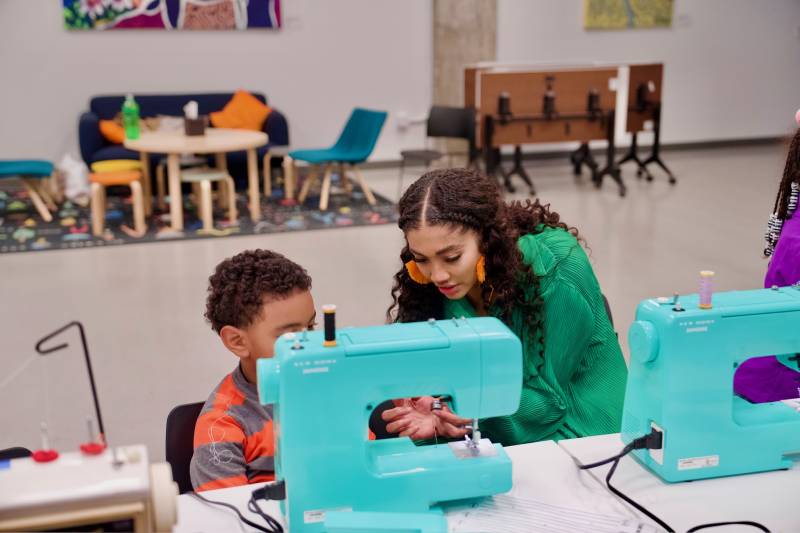 A woman teaches a young boy how to use a sewing machine.