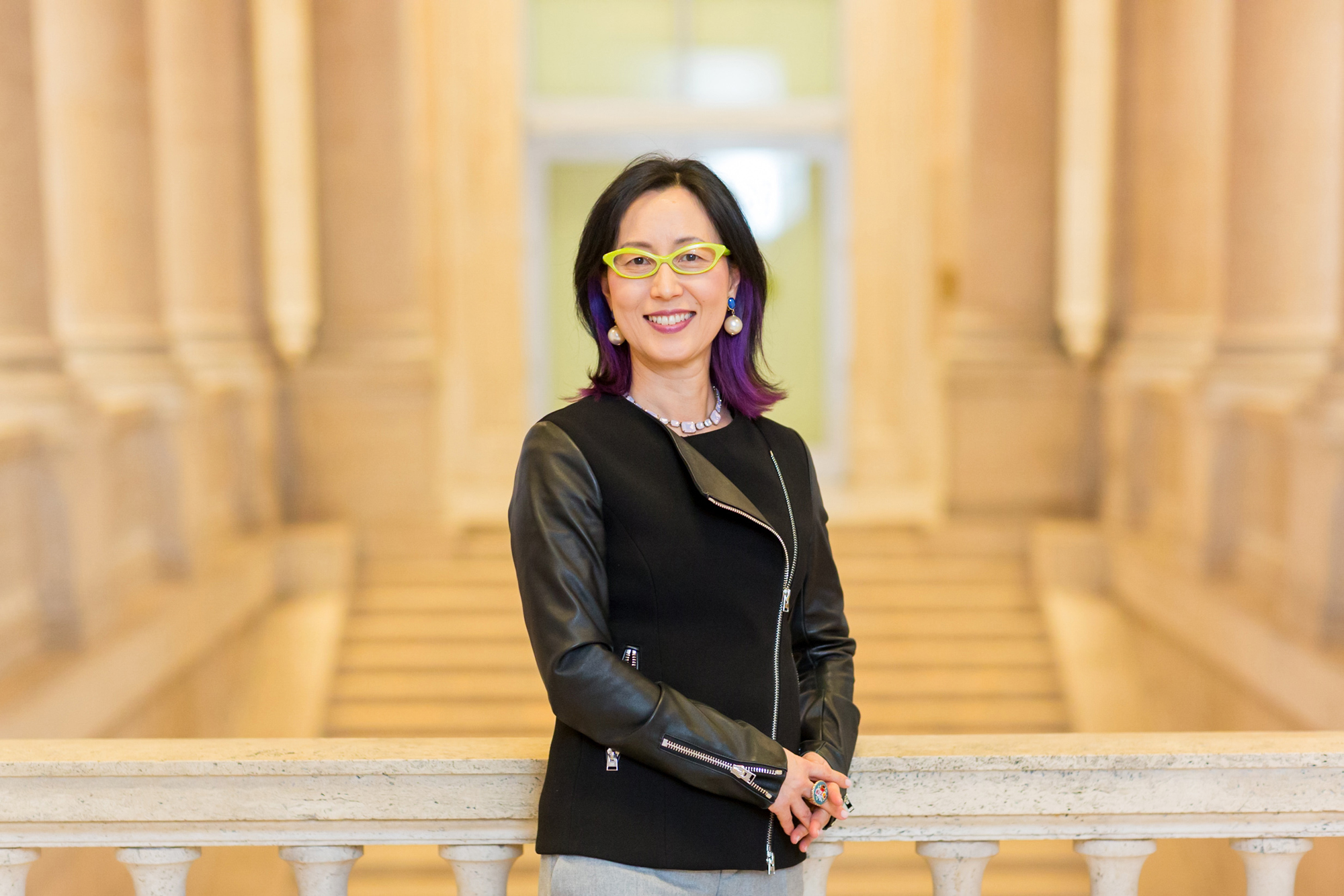 Asian woman stands smiling in grand white stone stairwell