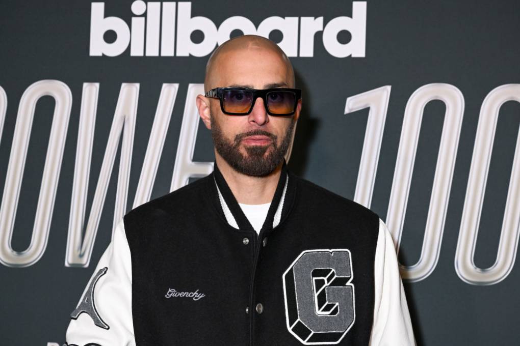 Ghazi poses on a red carpet wearing a jacket with a letter "G" and sunglasses.