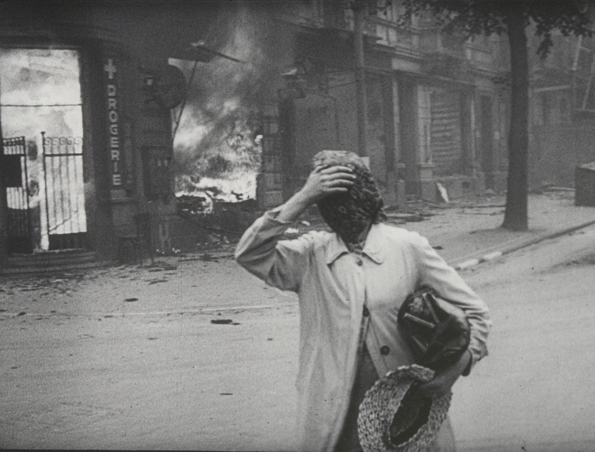 woman holds hand to head as a building burns behind her