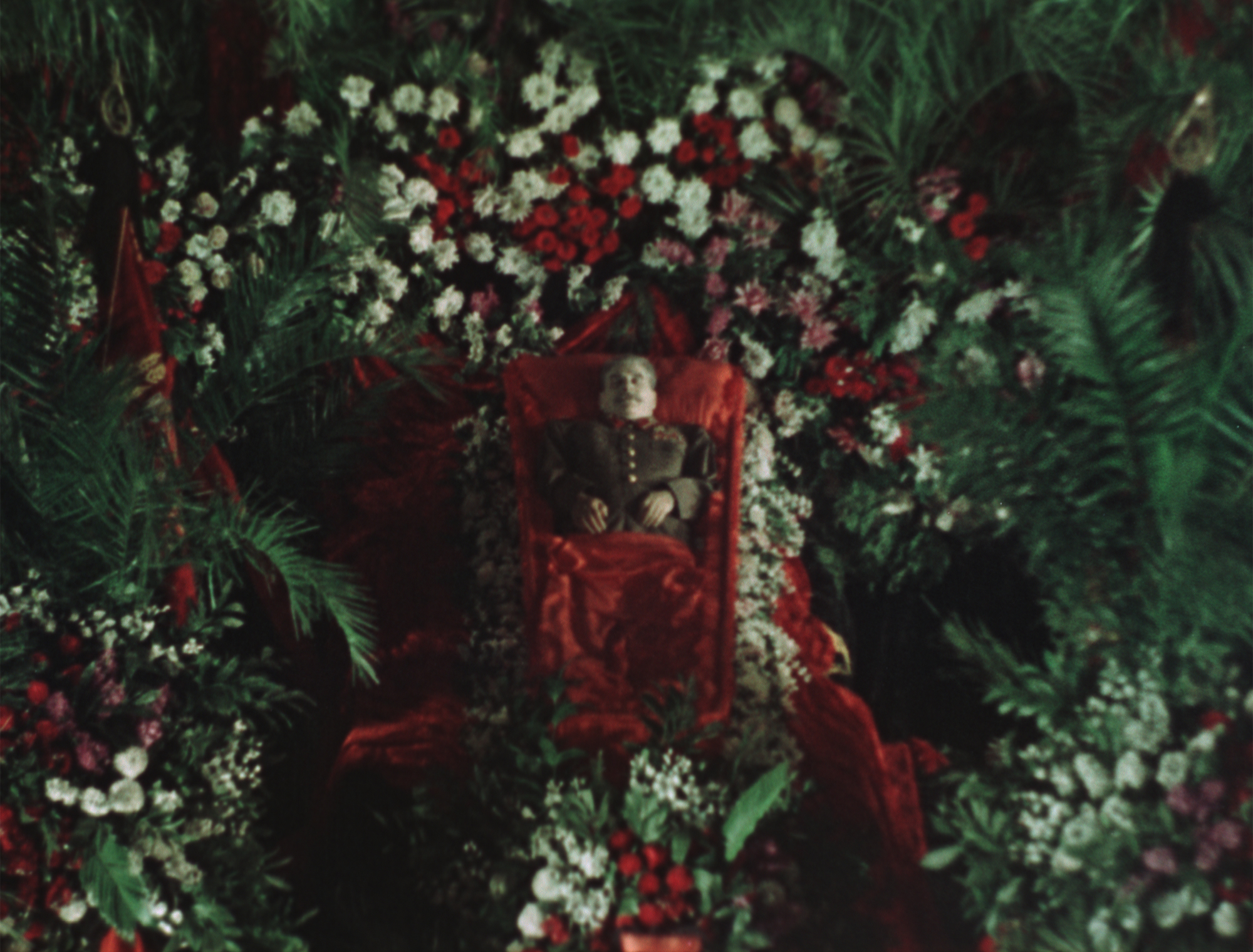 overhead view of man in red-lined coffin surrounded by hundreds of flowers