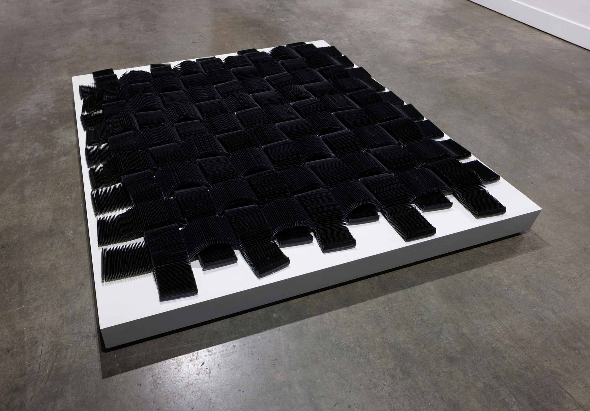 black plastic comb sculpture on low white pedestal
