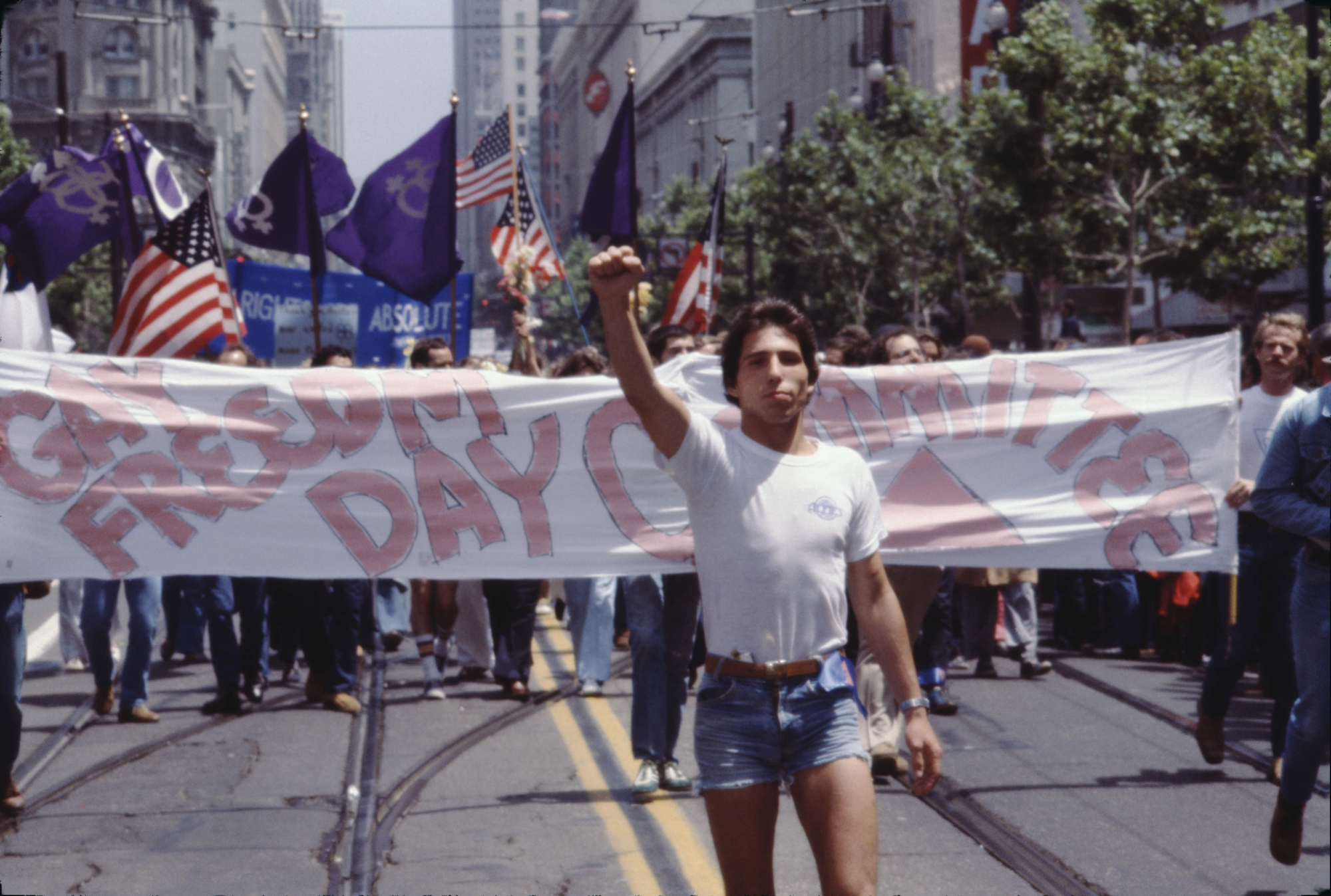 man marching in front of pride banner with raised first