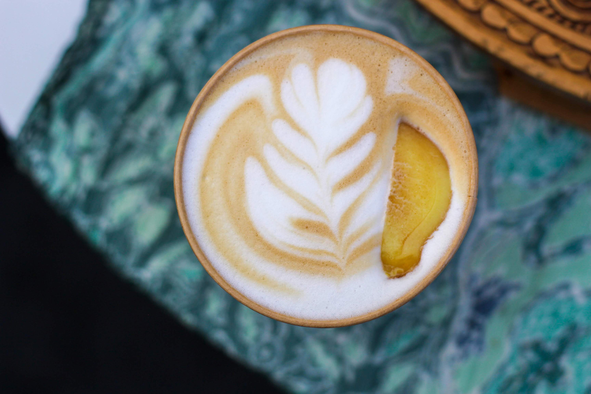 Overhead view of a latte with foam milk art, topped with a slice of roasted ginger.