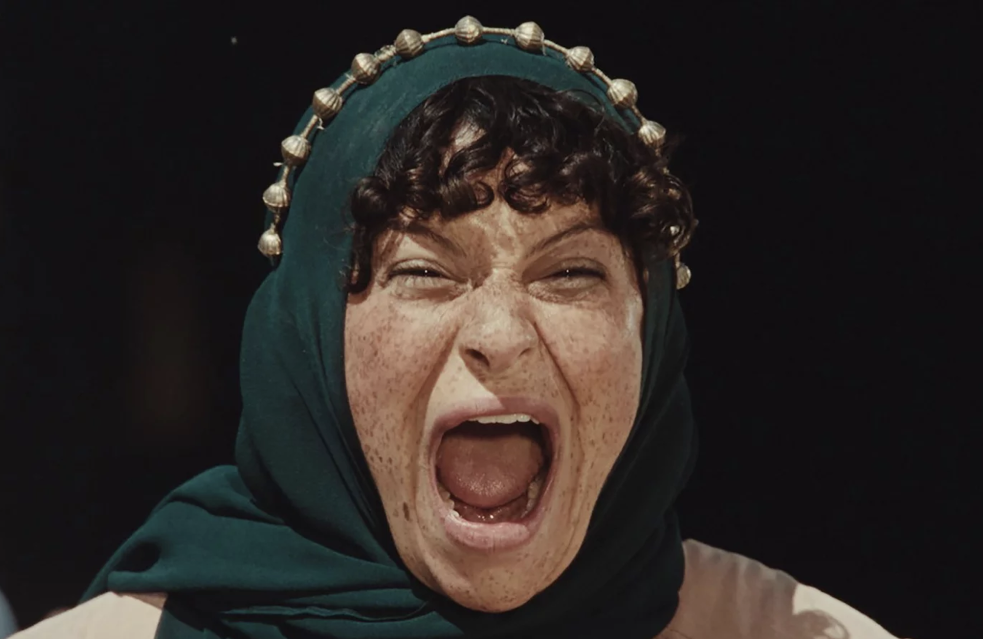 Close up of a woman with olive skin and freckles, wearing a hijab and screaming passionately.