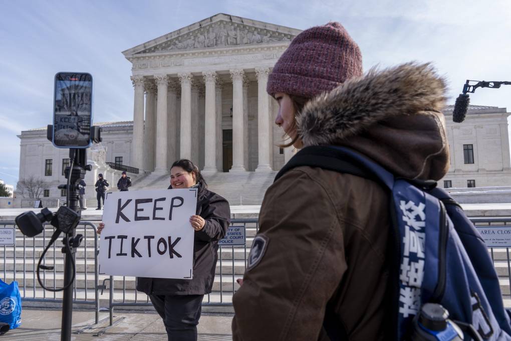 A woman carrying a large KEEP TIKTOK sign stands near a barrier outside the US Supreme Court while another woman wearing a winter coat watches on.