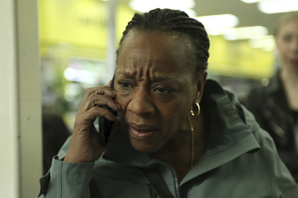 An older Black woman stands in a doorway, frowning while listening to a cell phone.