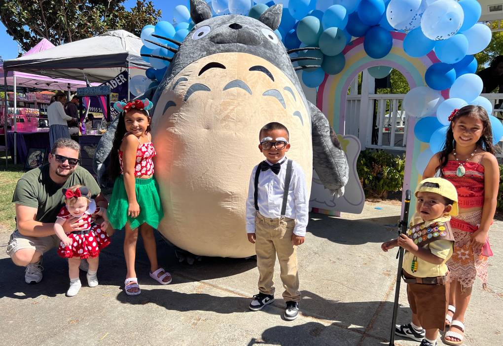 Children dressed up as Pixar and Disney characters pose in front of a giant stuffed Totoro.