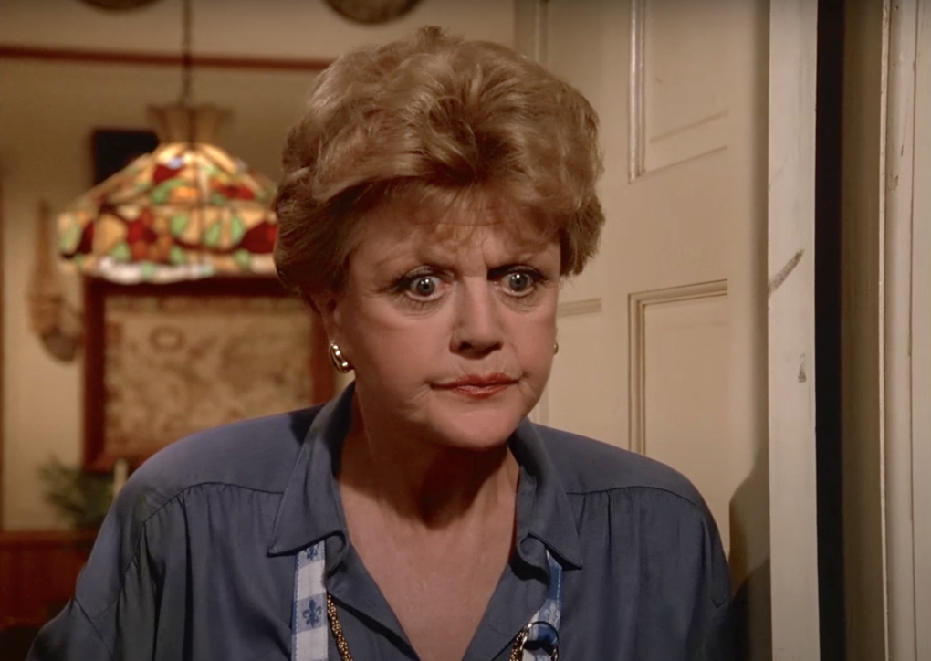 A senior woman with short tousled hair stands in a doorway looking perturbed.
