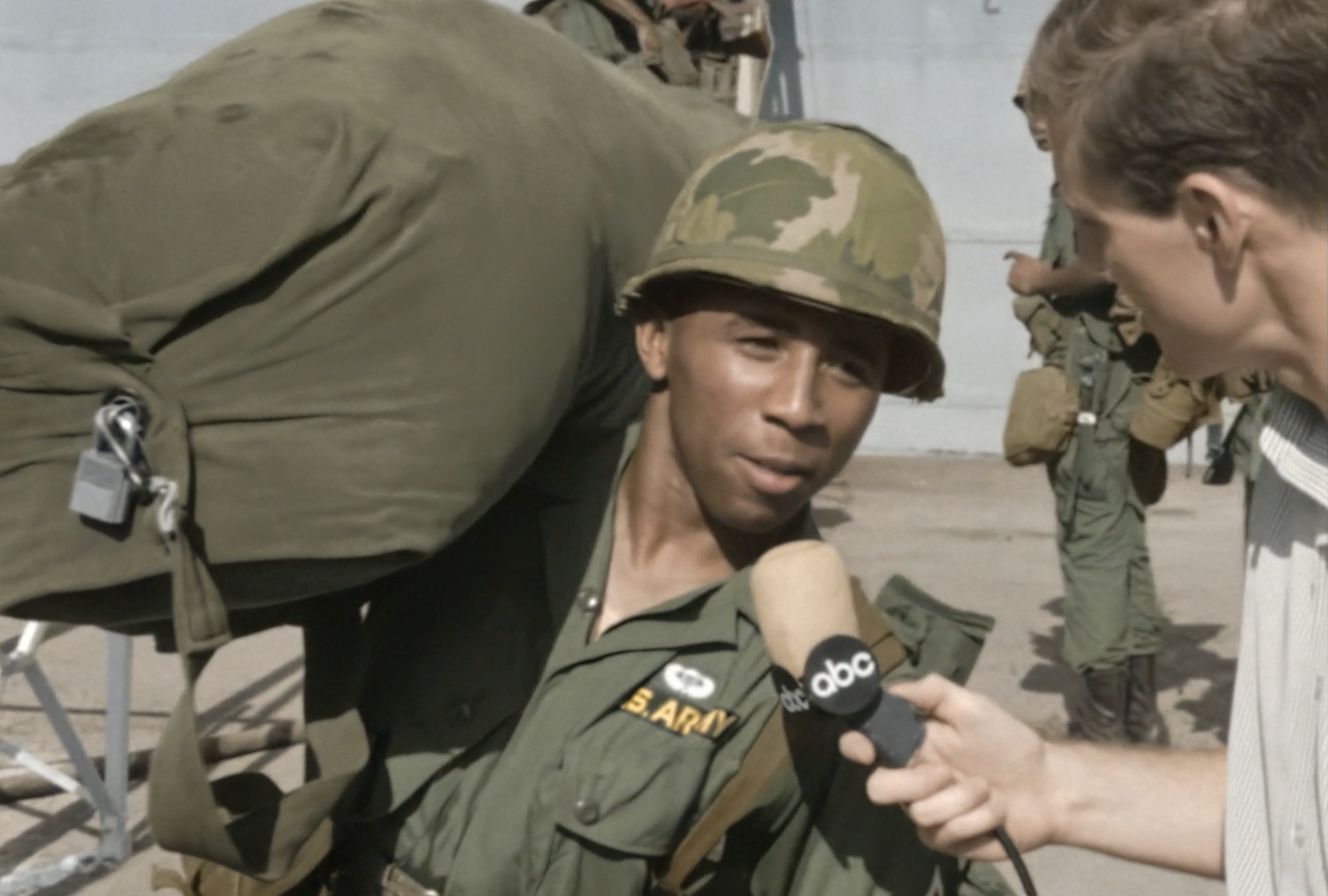 A young Black man in a US Army uniform carries a heavy bag on his shoulder and stops to talk to a news journalist from abc.