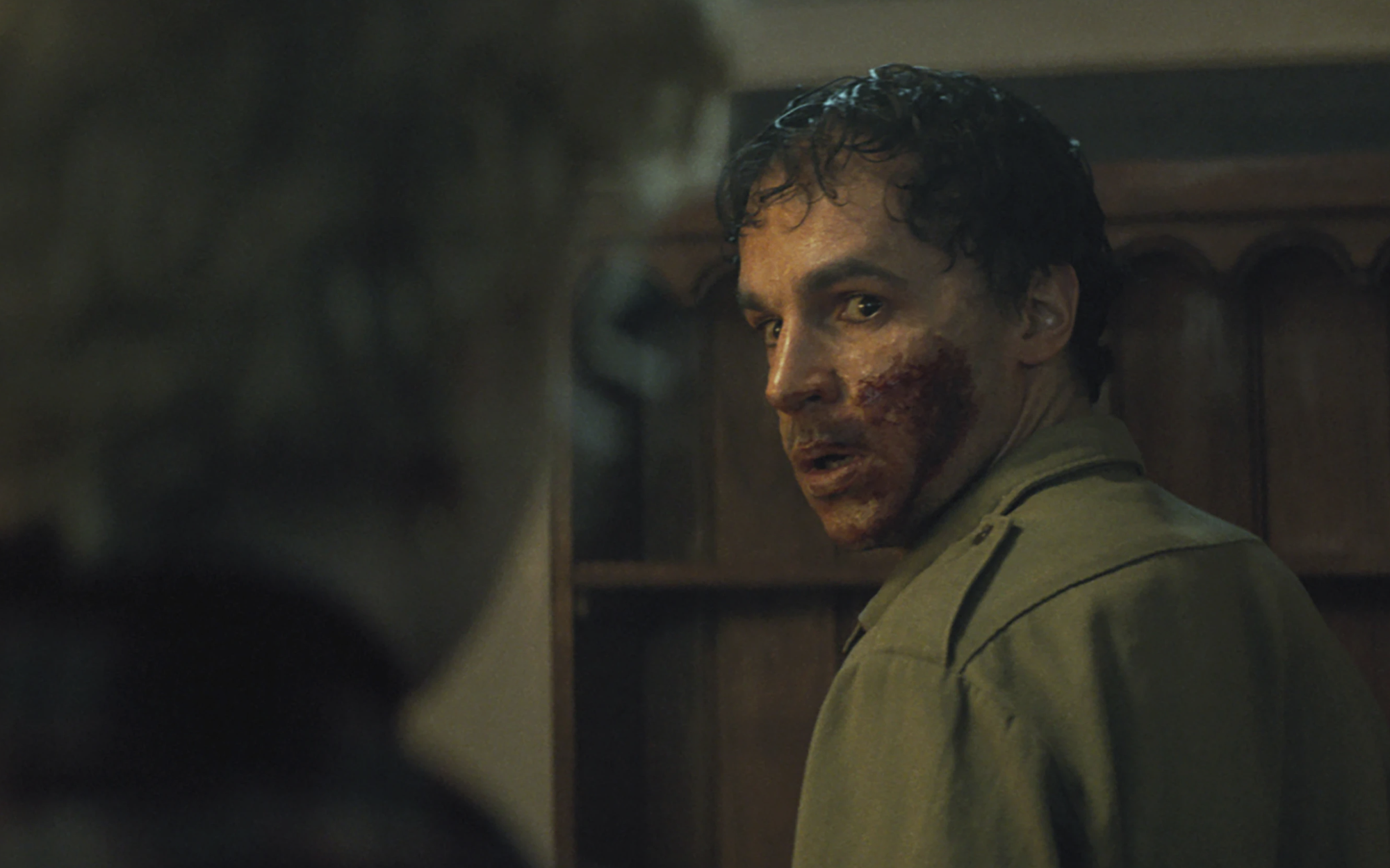 A white man with a bloodied face and dirty hair glances over his shoulder at a woman.