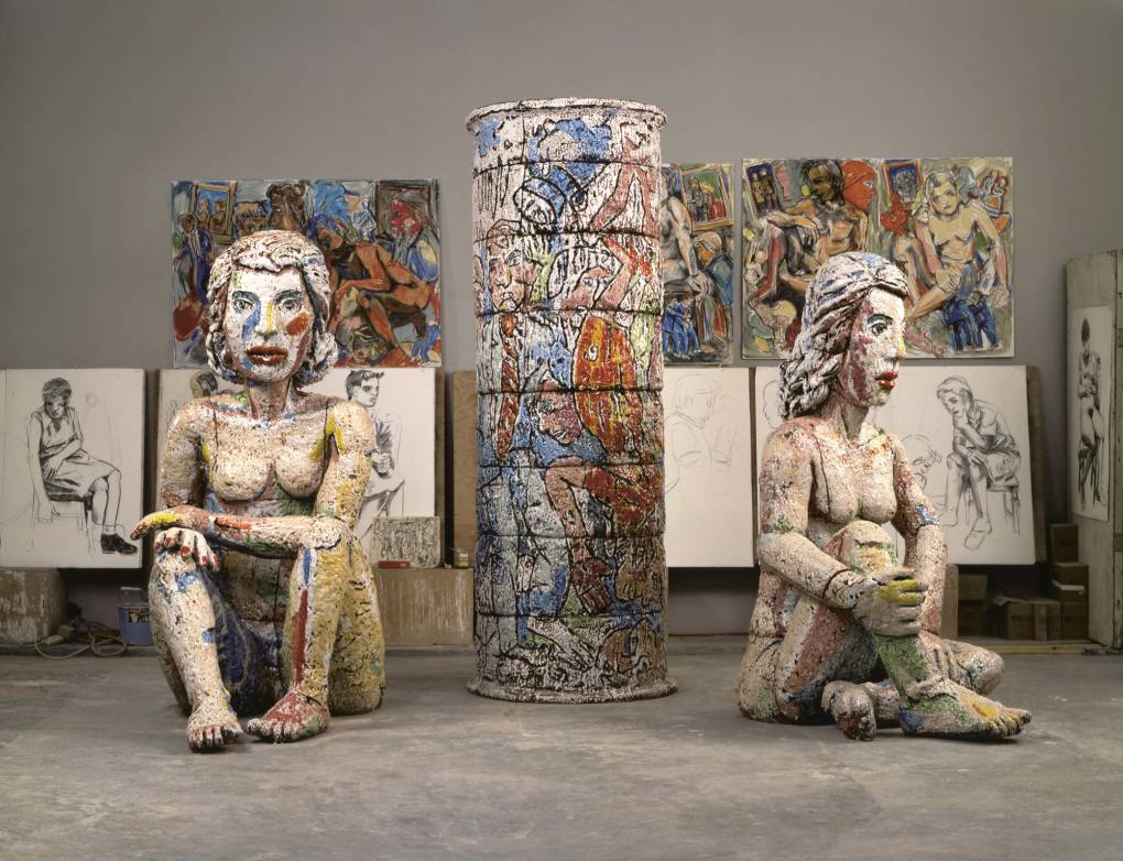 two large seated figurative sculptures arranged in front of sketches and more ceramics