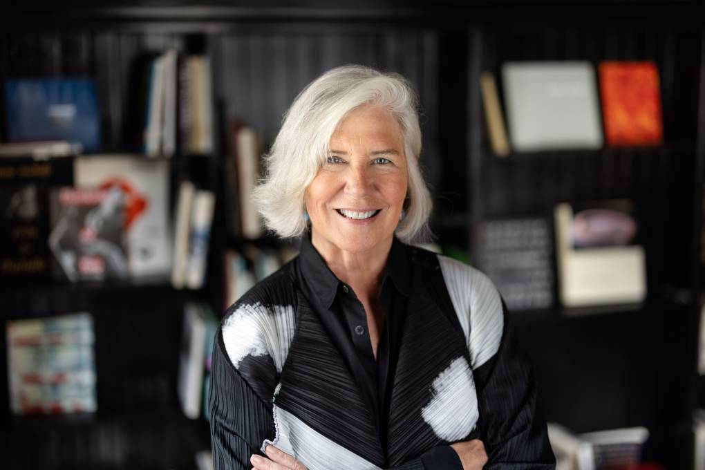 white woman with white hair smiling, arms crossed