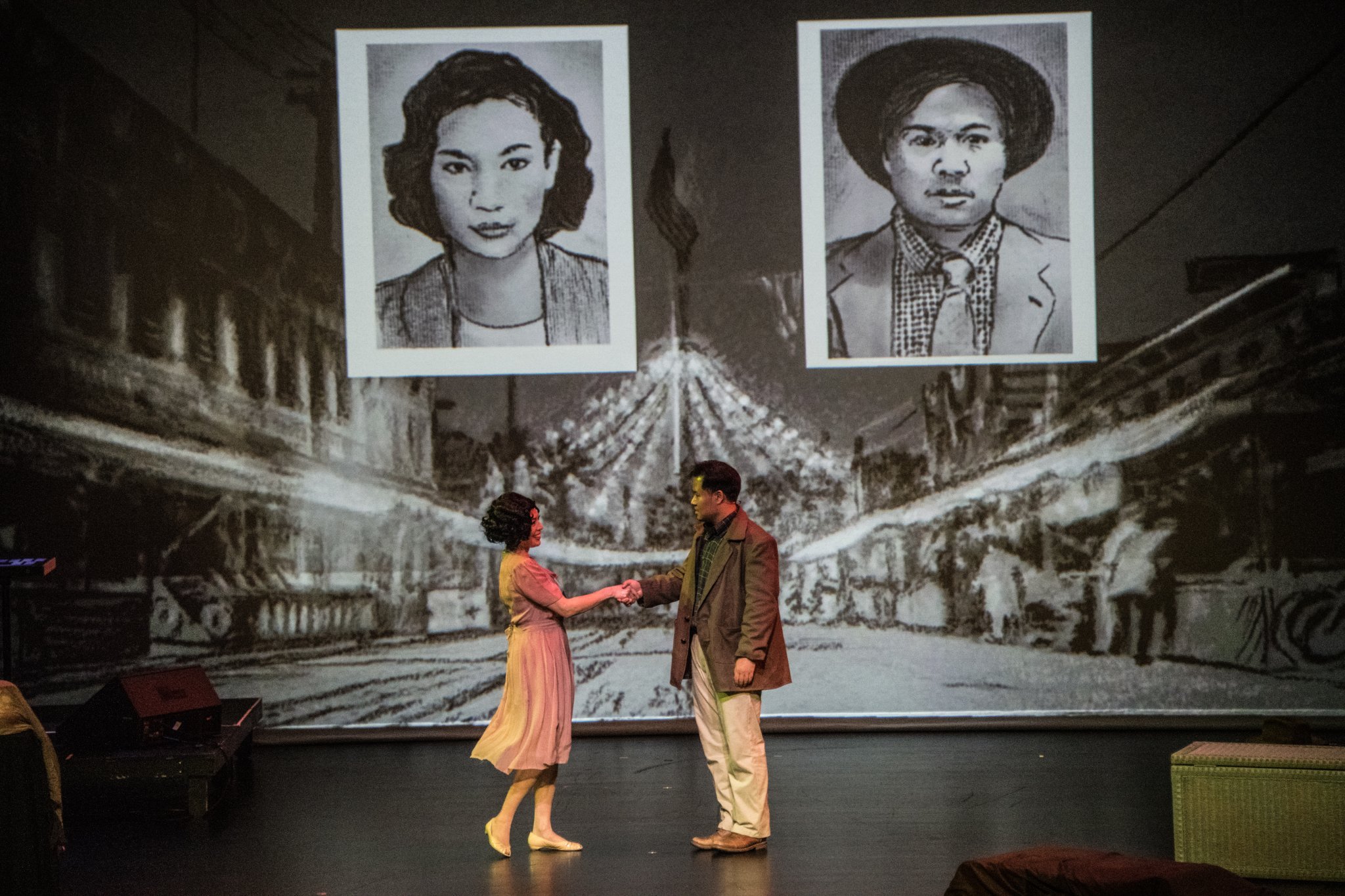 woman and man shake hands on stage under large ID images projected behind them
