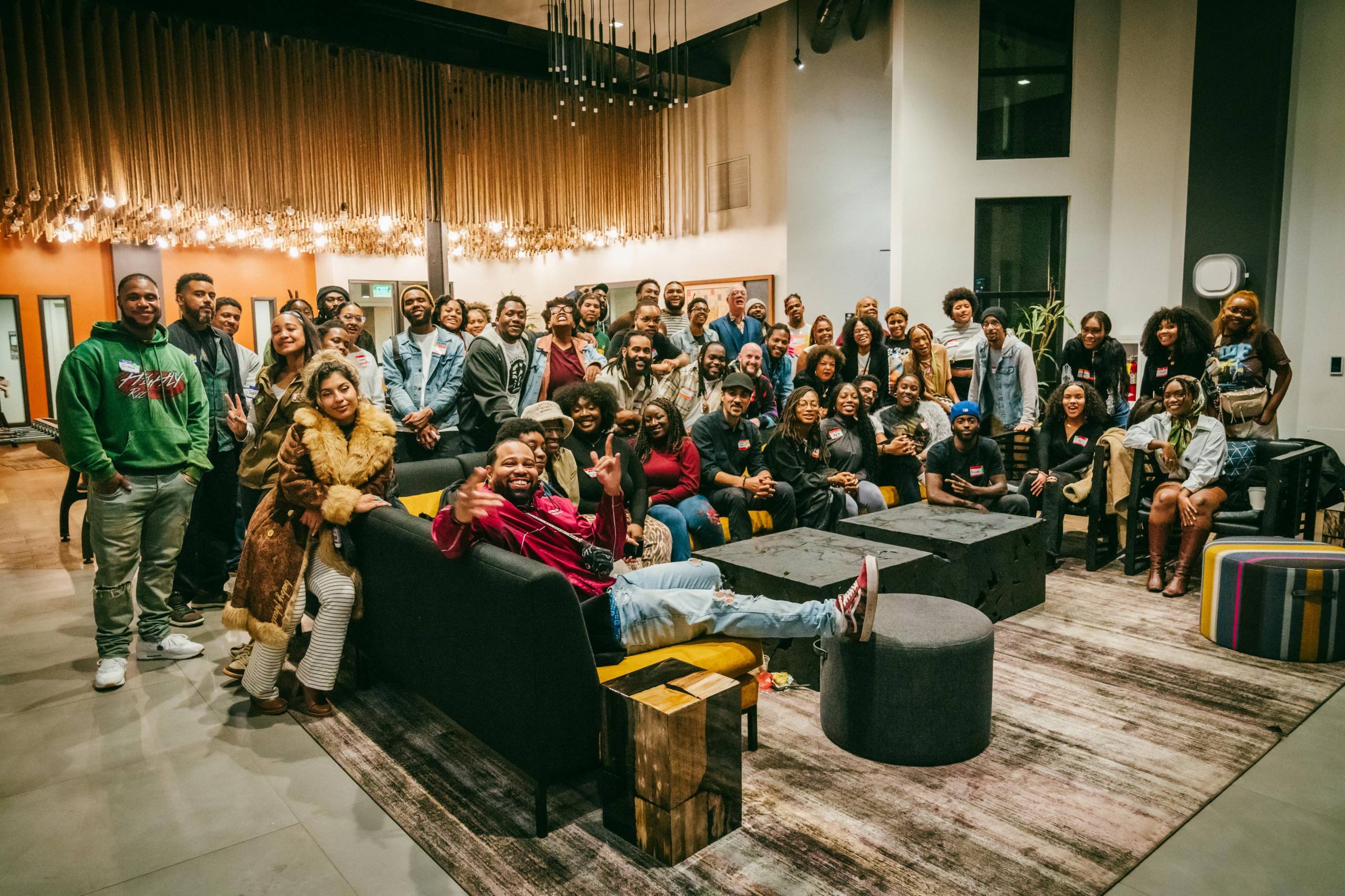 A group of over 25 people gather around a couch as they pose for a photo.