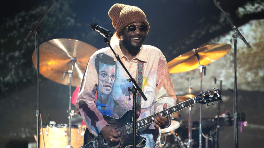 Gary Clark Jr. smiles as he strums his guitar.