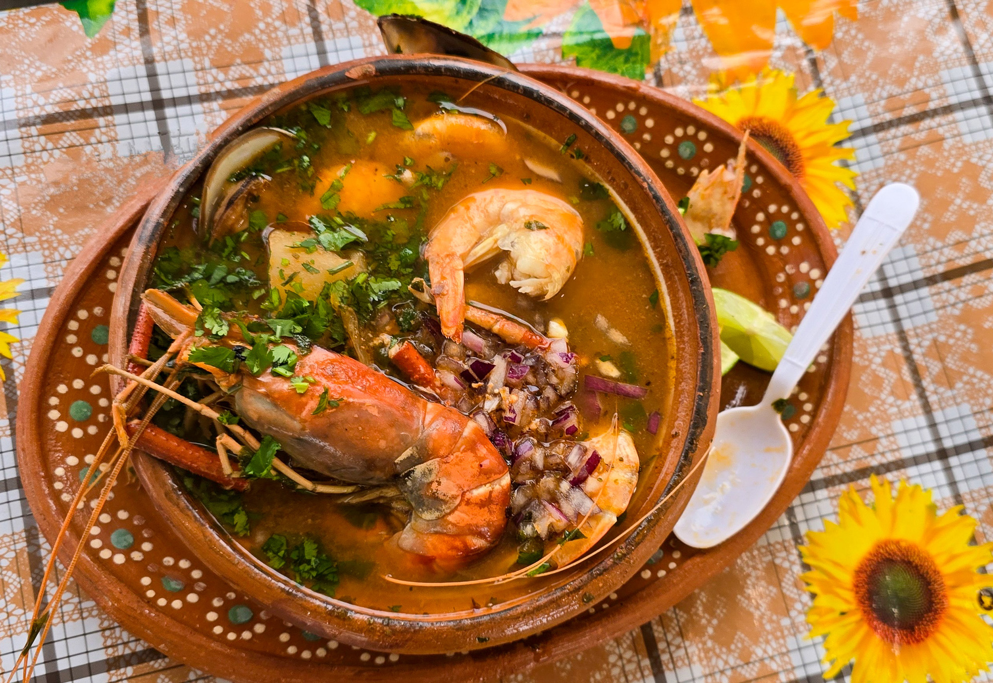 A bowl of soup filled with large shrimp, garnished with chopped onion and cilantro.