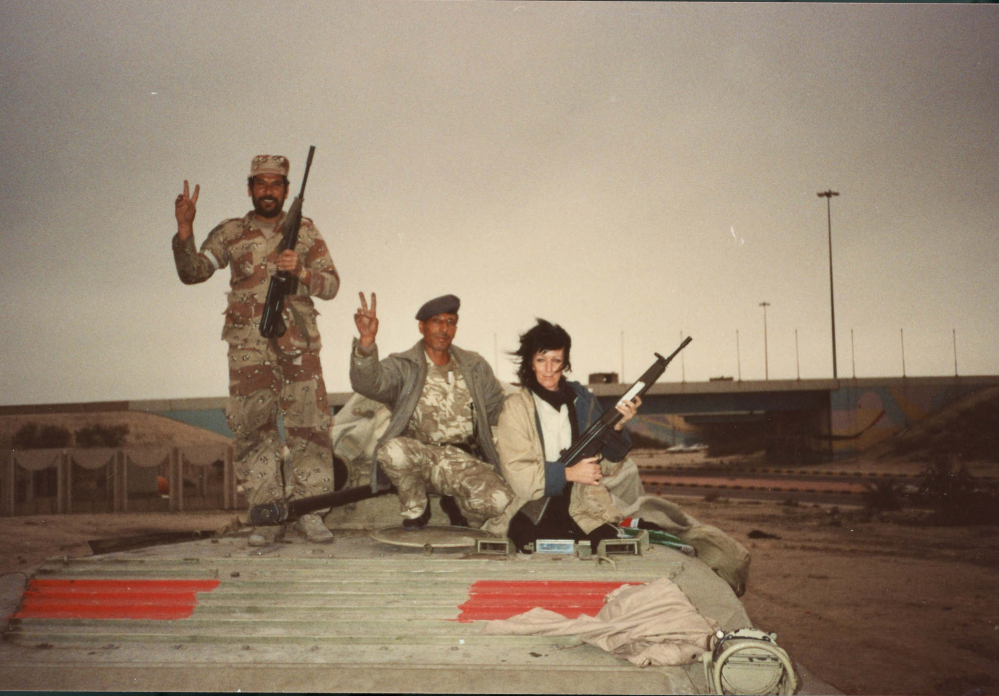 two men in military uniforms and a woman pose with peace signs and guns