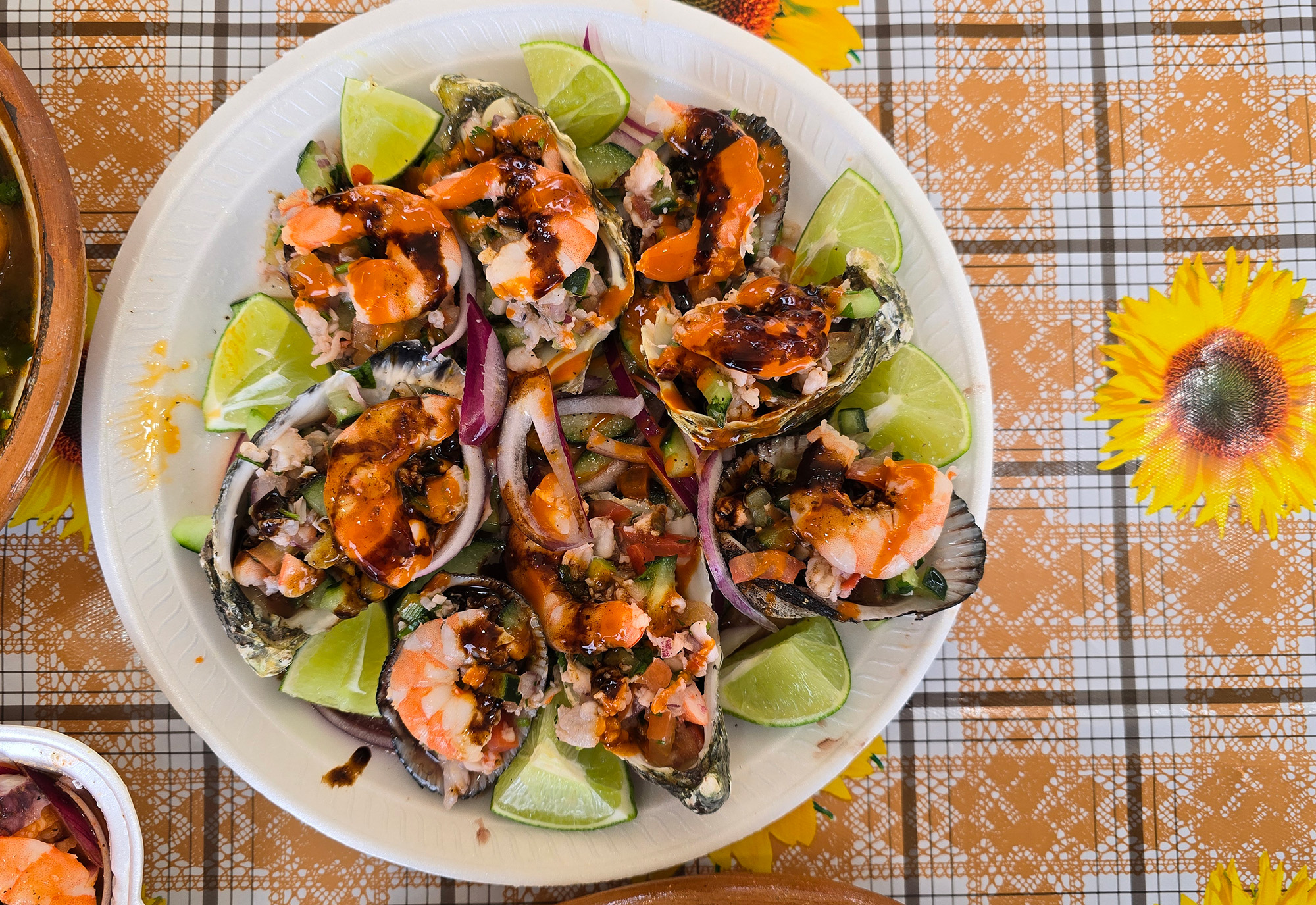 Overhead view of a large platter of clams and oysters topped with shrimp, with lime wedges all around the perimeter of the plate.