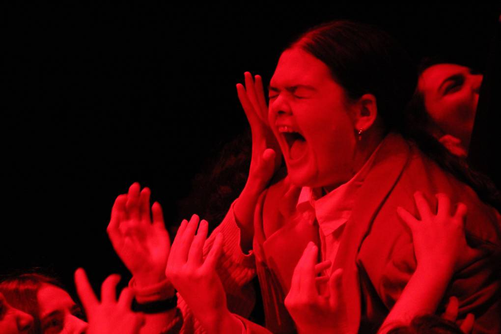 A young woman in red light screams as hands protrude around her from below