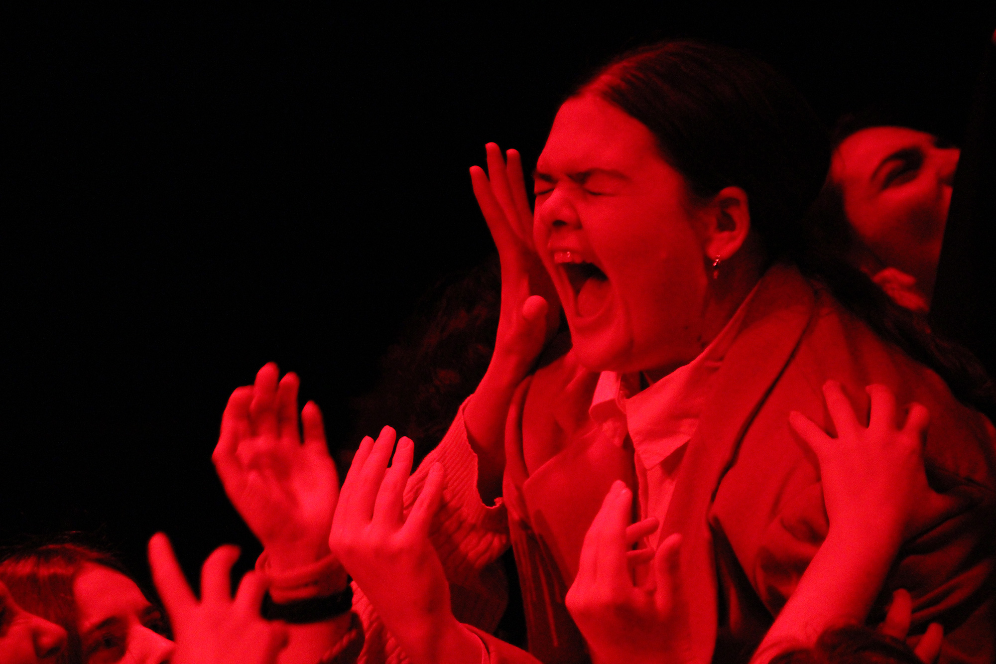 A young woman in red light screams as hands protrude around her from below