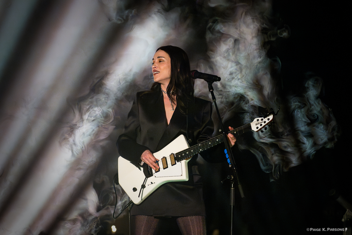 Woman on stage with white electric guitar and shafts of light behind