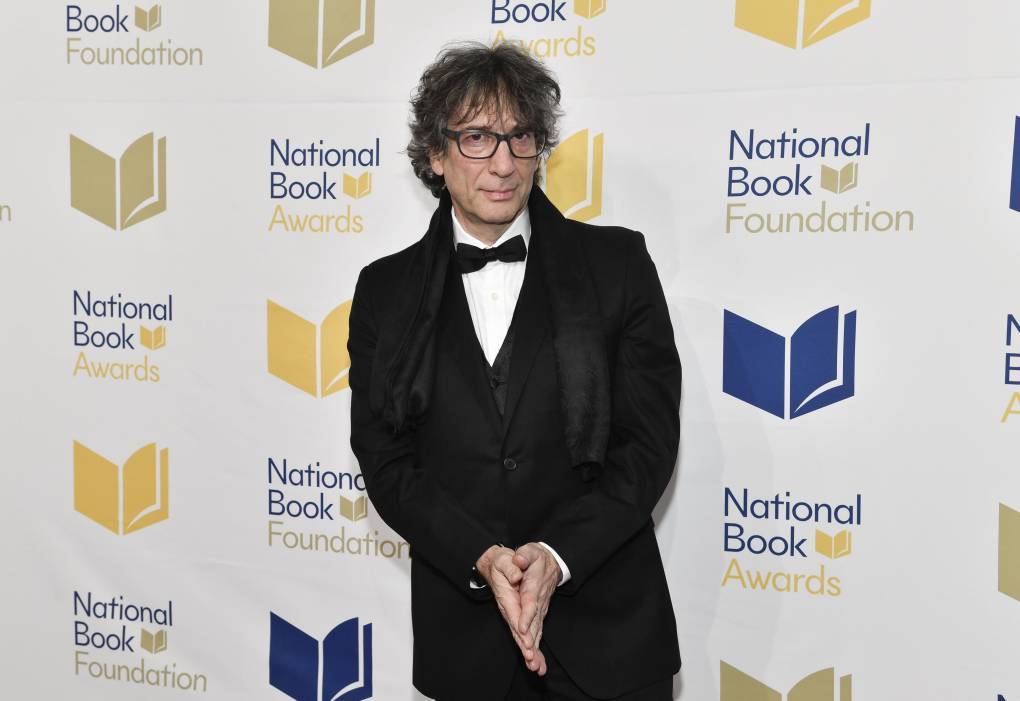 A middle aged man with glasses and disheveled black hair, wearing a black suit and bow tie on a red carpet.