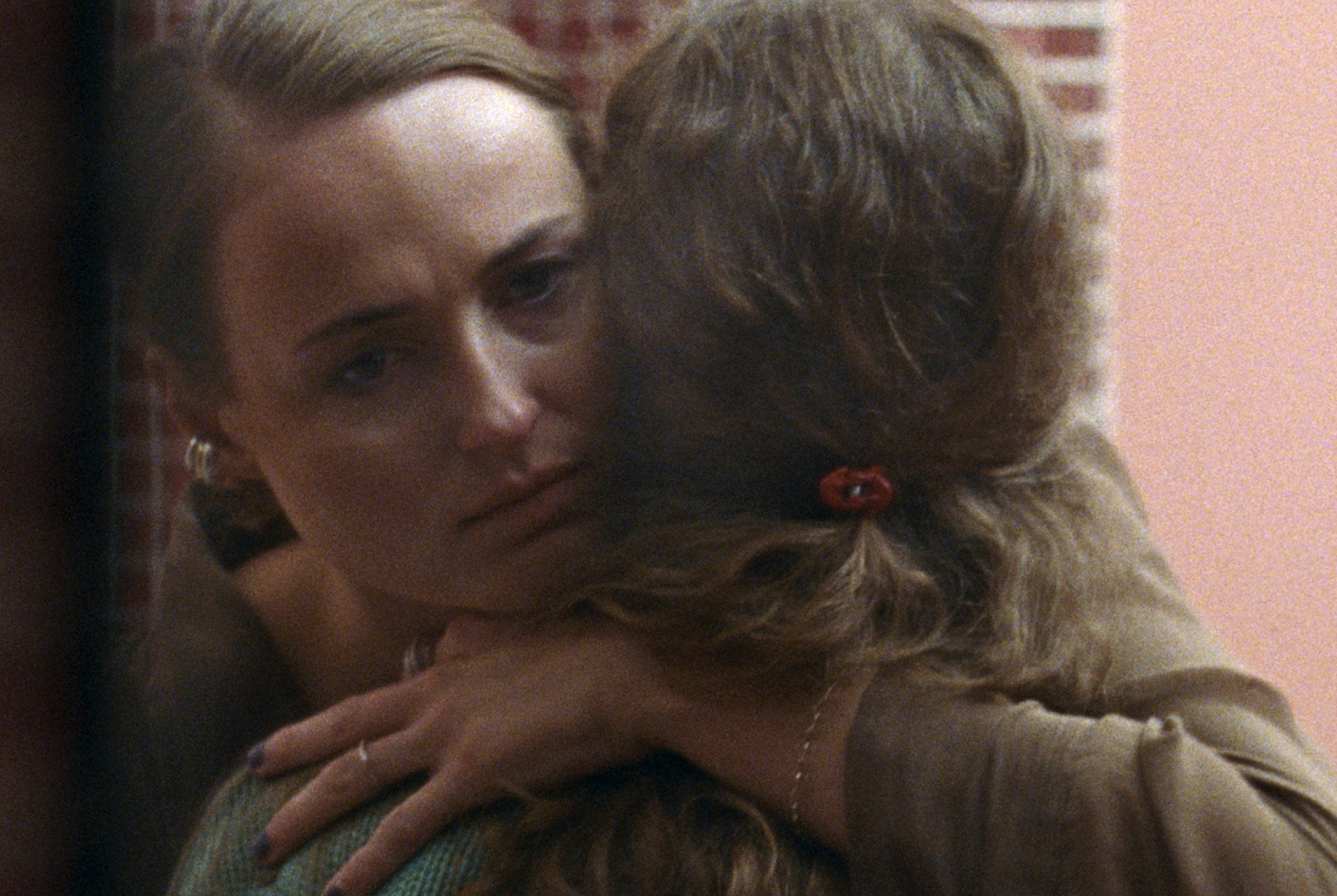 A woman's forlorn face is visible as she embraces a second woman whose back is to the camera.