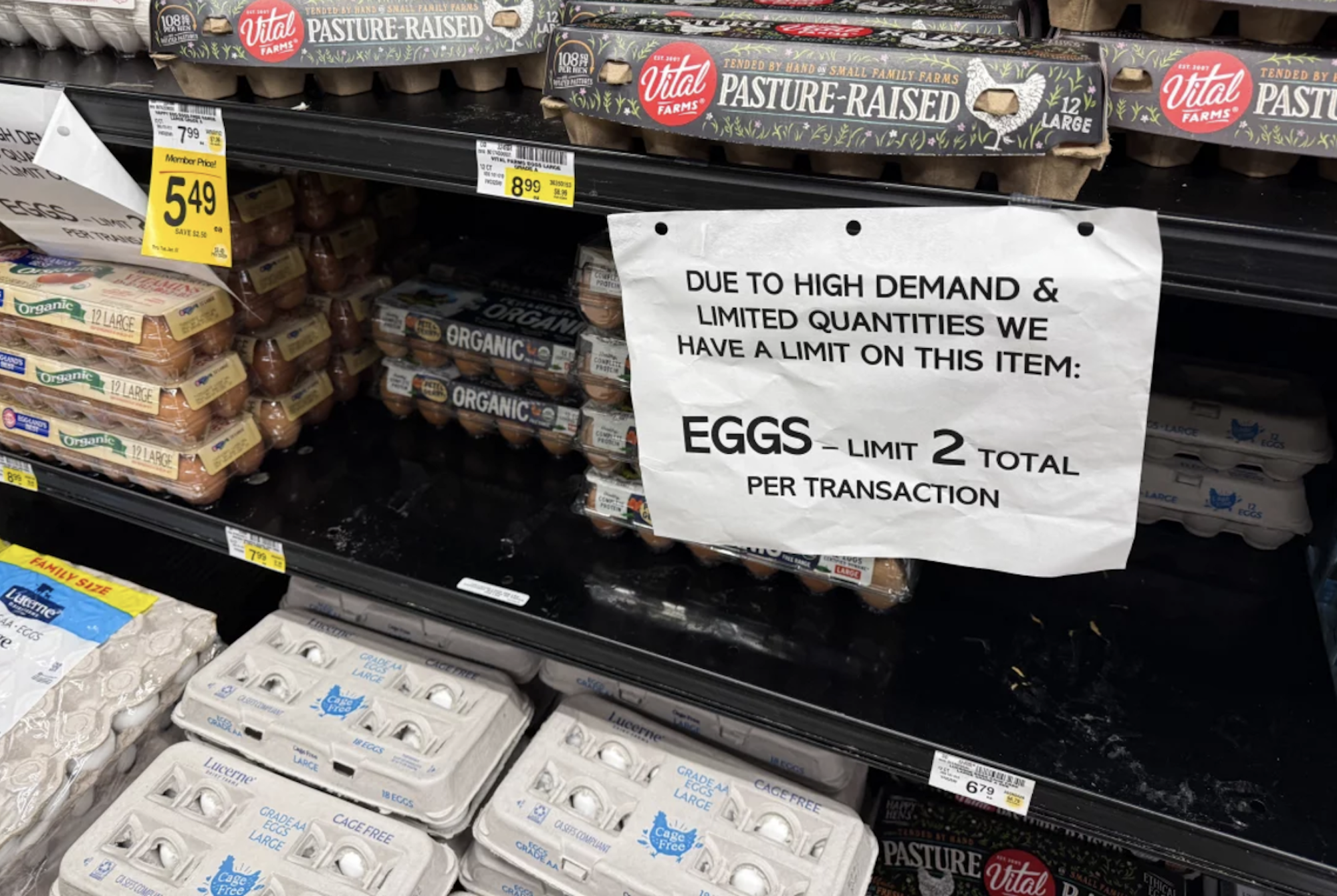 Boxes of eggs on a grocery shelf alongside a sign instructing shoppers they are limited to two boxes only.