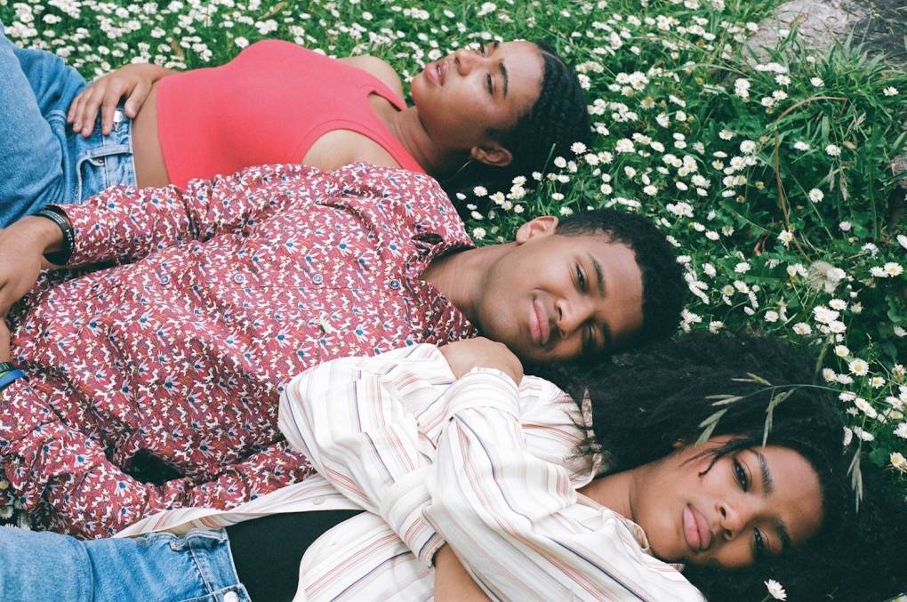 Three siblings lie together in the grass.