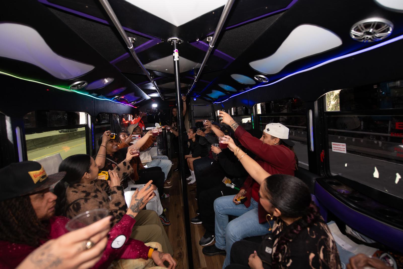 People sit on a bus, holding drinking glasses up as they celebrate.