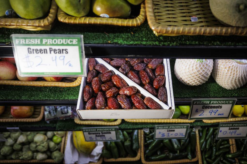 A box of dates in a produce display, between trays of apples and coconuts.