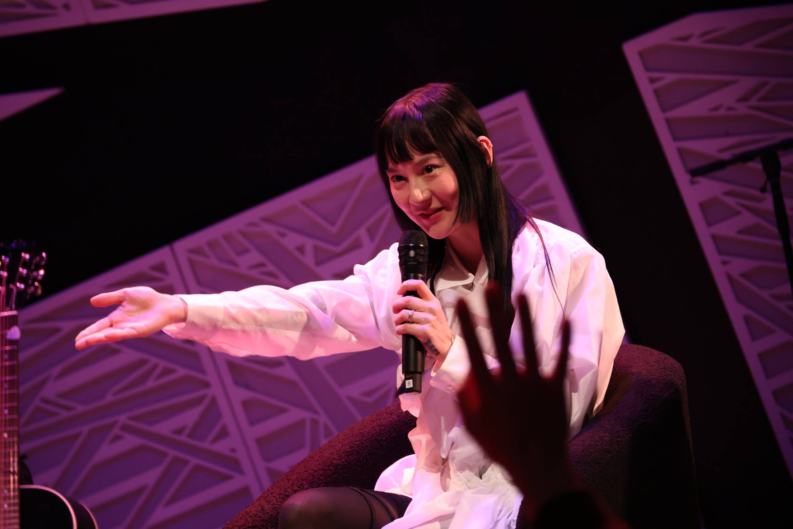 woman in white holds mic to face and gestures out to crowd