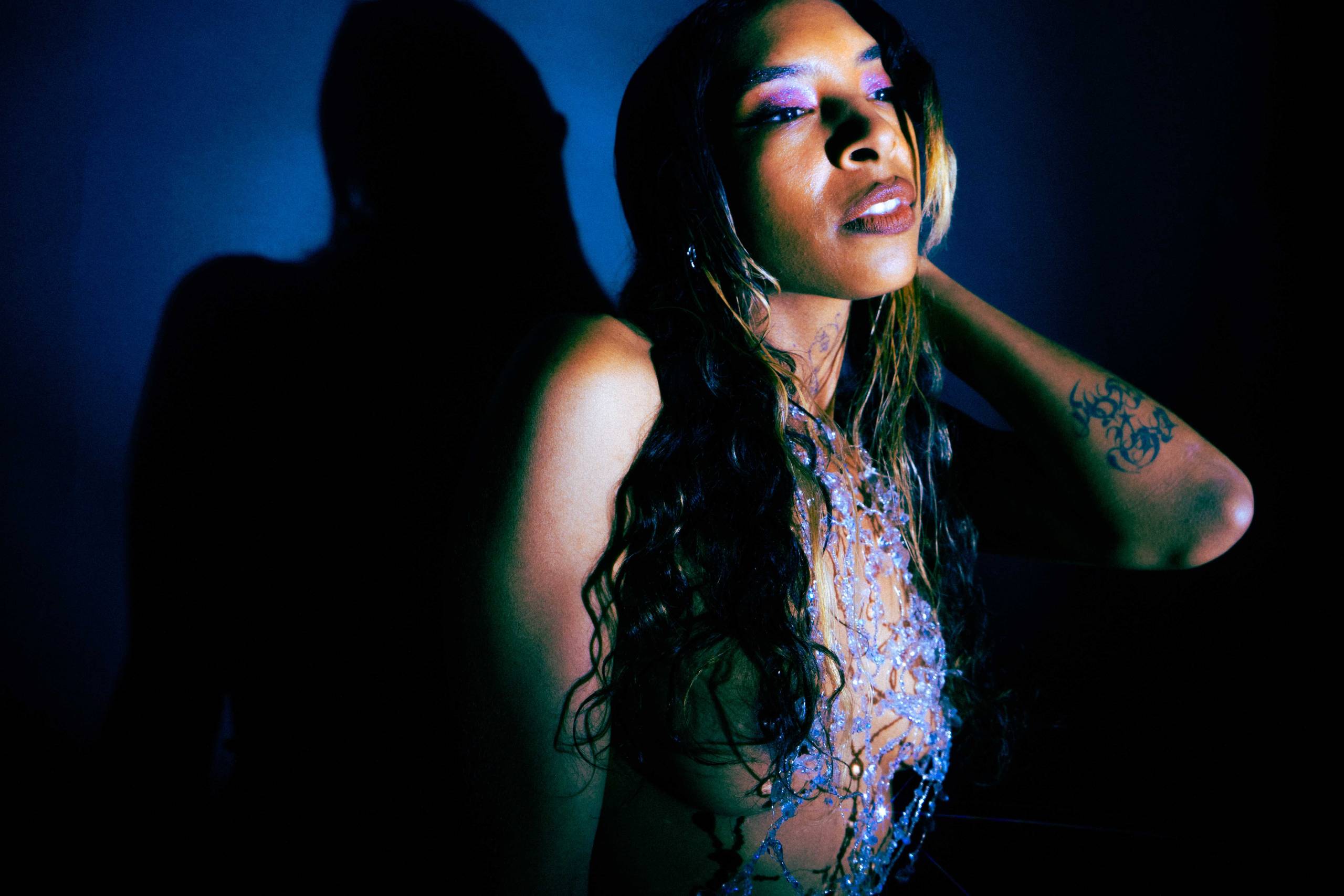 A portrait of SPELLLING in a dark room illuminated by a spotlight.