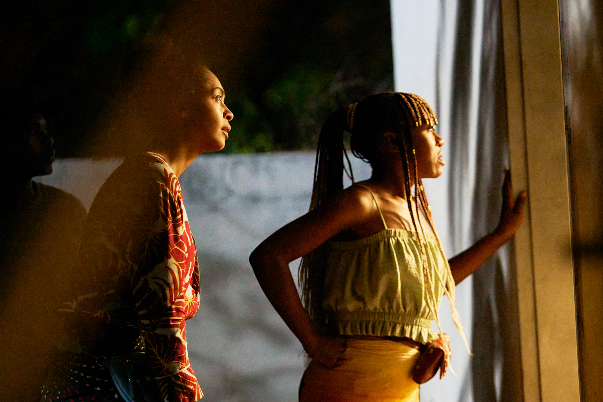 two women stand looking out window, tense