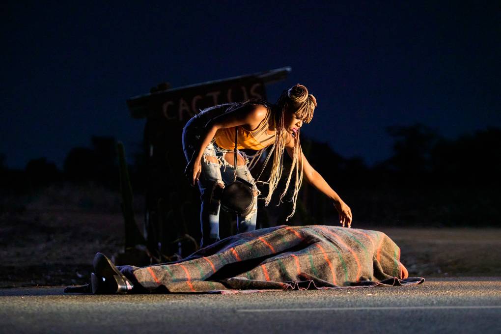 Woman leans over covered body on ground, touches it gingerly