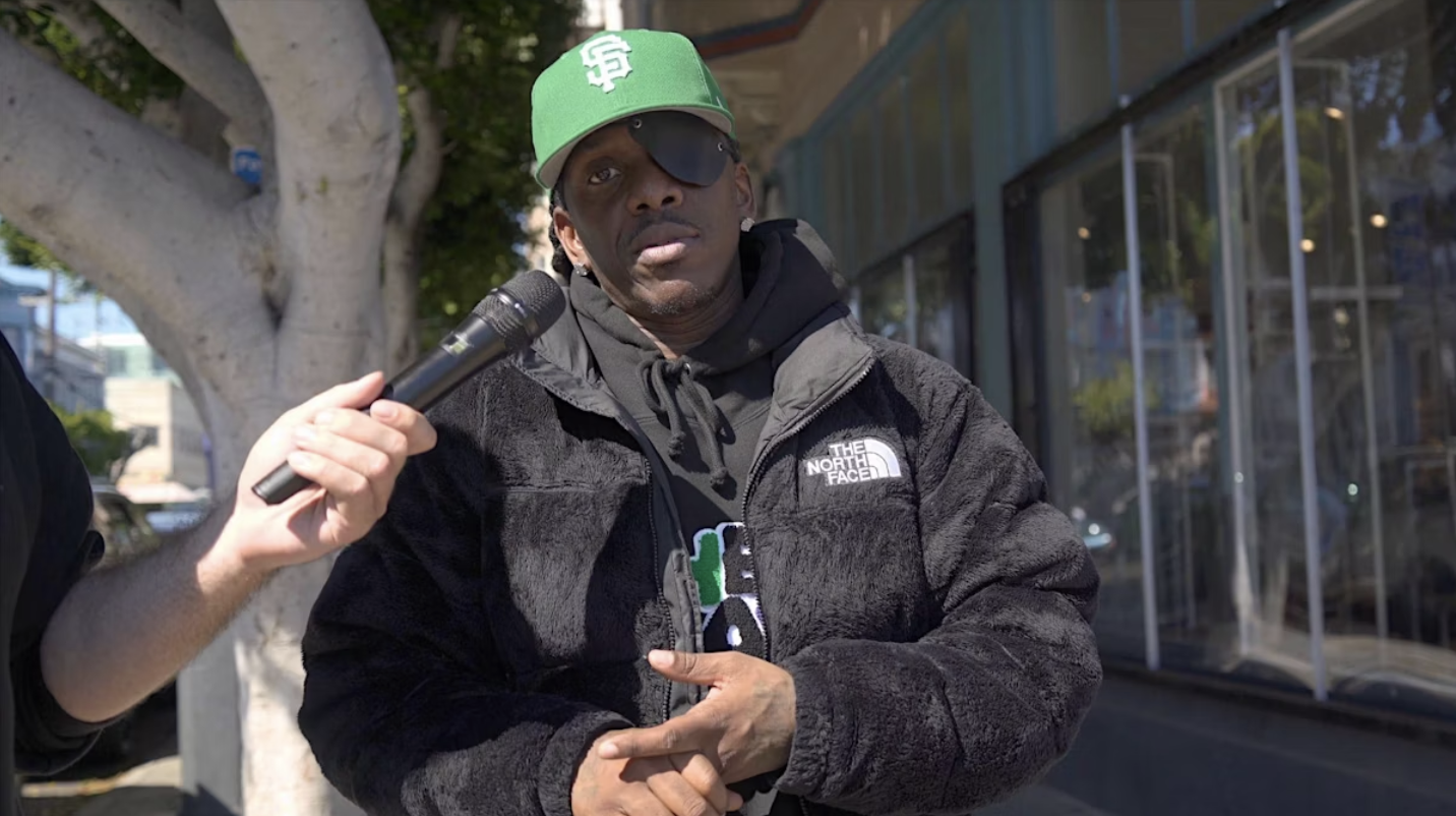 A man speaks into a microphone during a street interview.