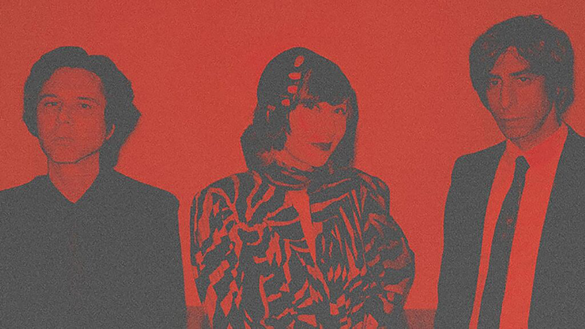 Three people, elegantly dressed, stand against a red background