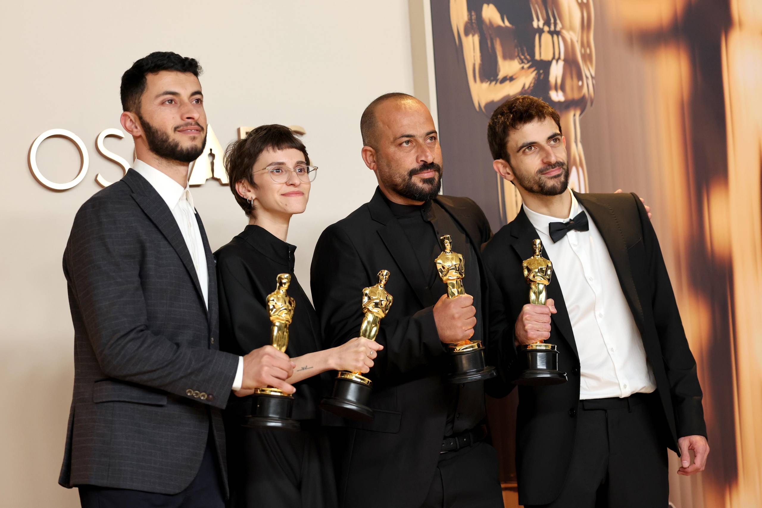 Four people in formal wear hold Oscar statuettes