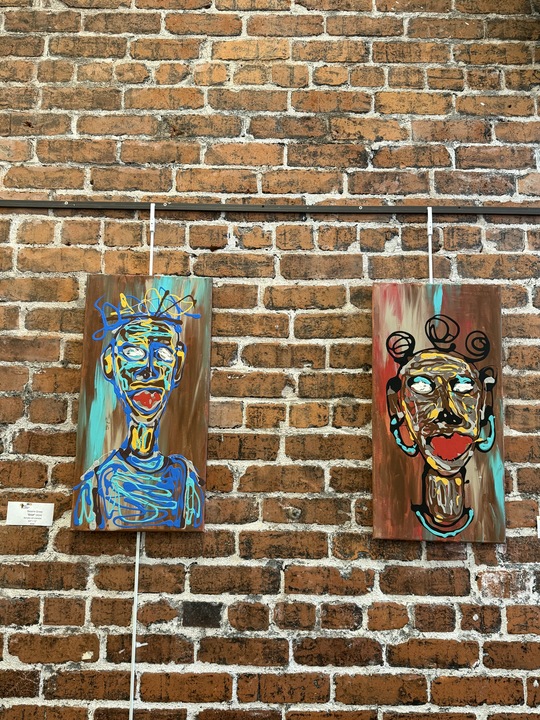 Two paintings of faces mounted on a brick wall.