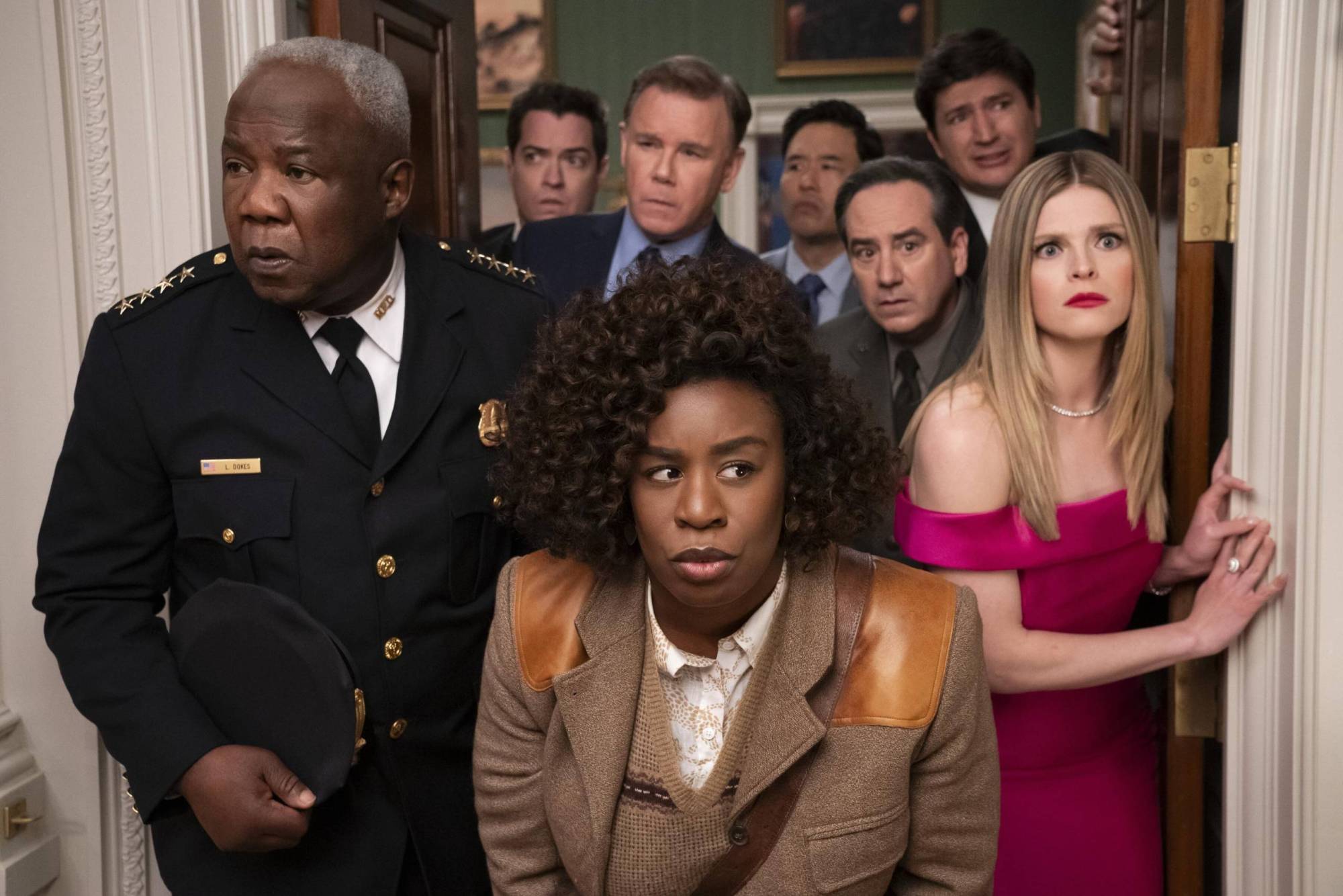 A Black woman wearing a tweed suit peers through a door suspiciously, as seven men and women gather behind her, wearing similar expressions.