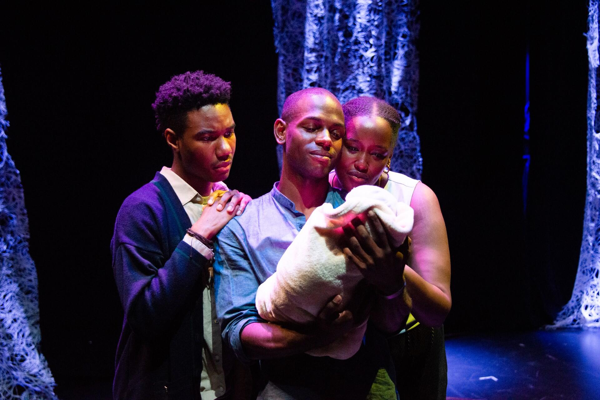 three people on stage hold a baby and smile
