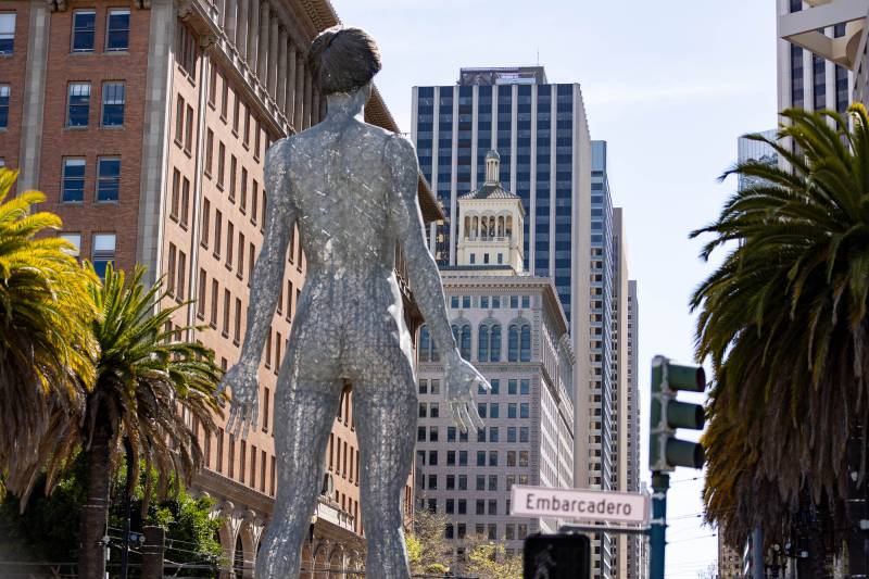 view of backside of giant metal sculpture of nude woman, looking down Market Street