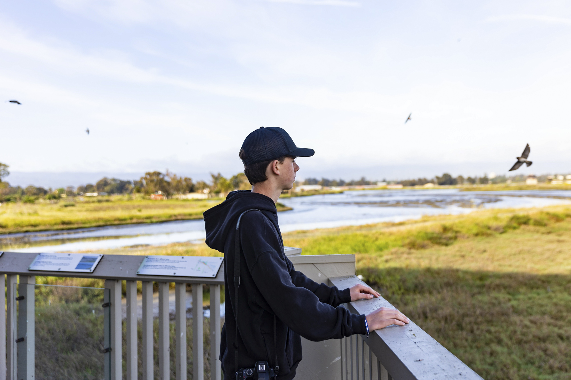 young person in cap stands at railing overlooking wetlands