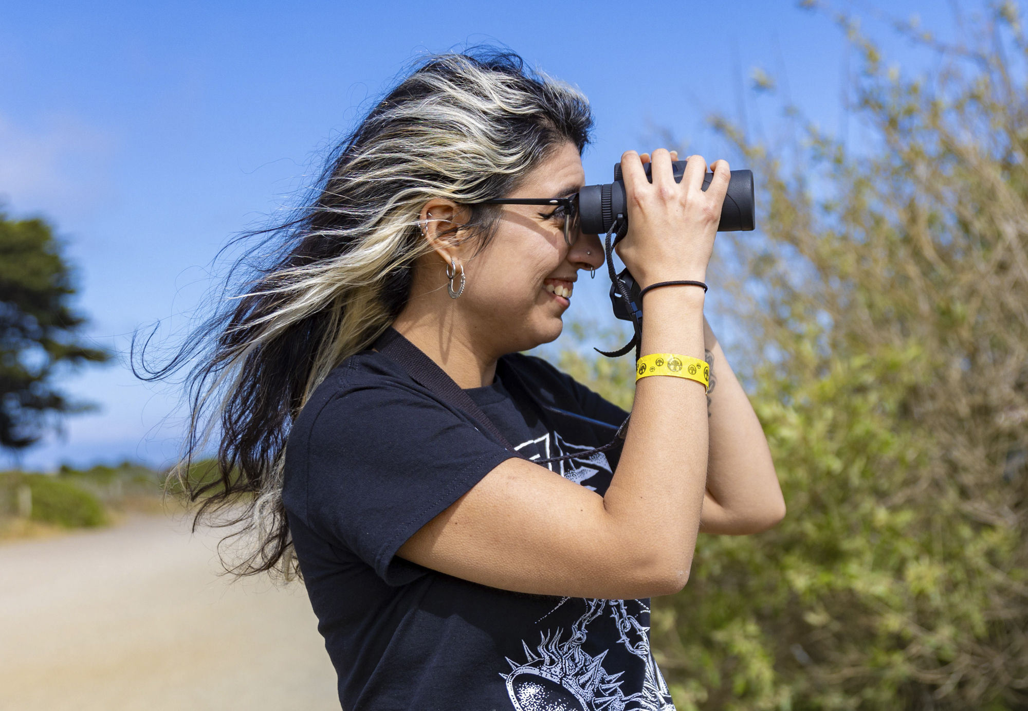 woman looks through binoculars, wind in hair