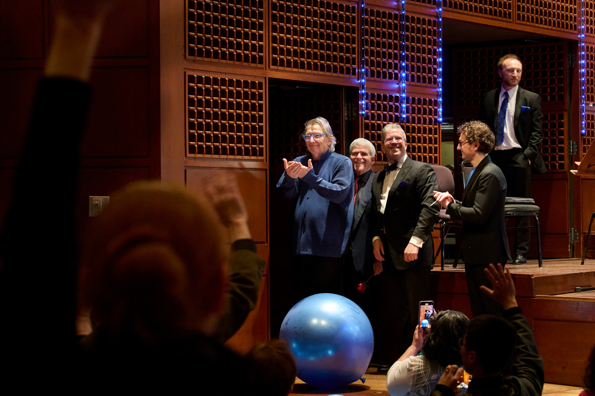 A man in a blue shirt clasps his hands in appreciation next to a door as smiling friends stand close by