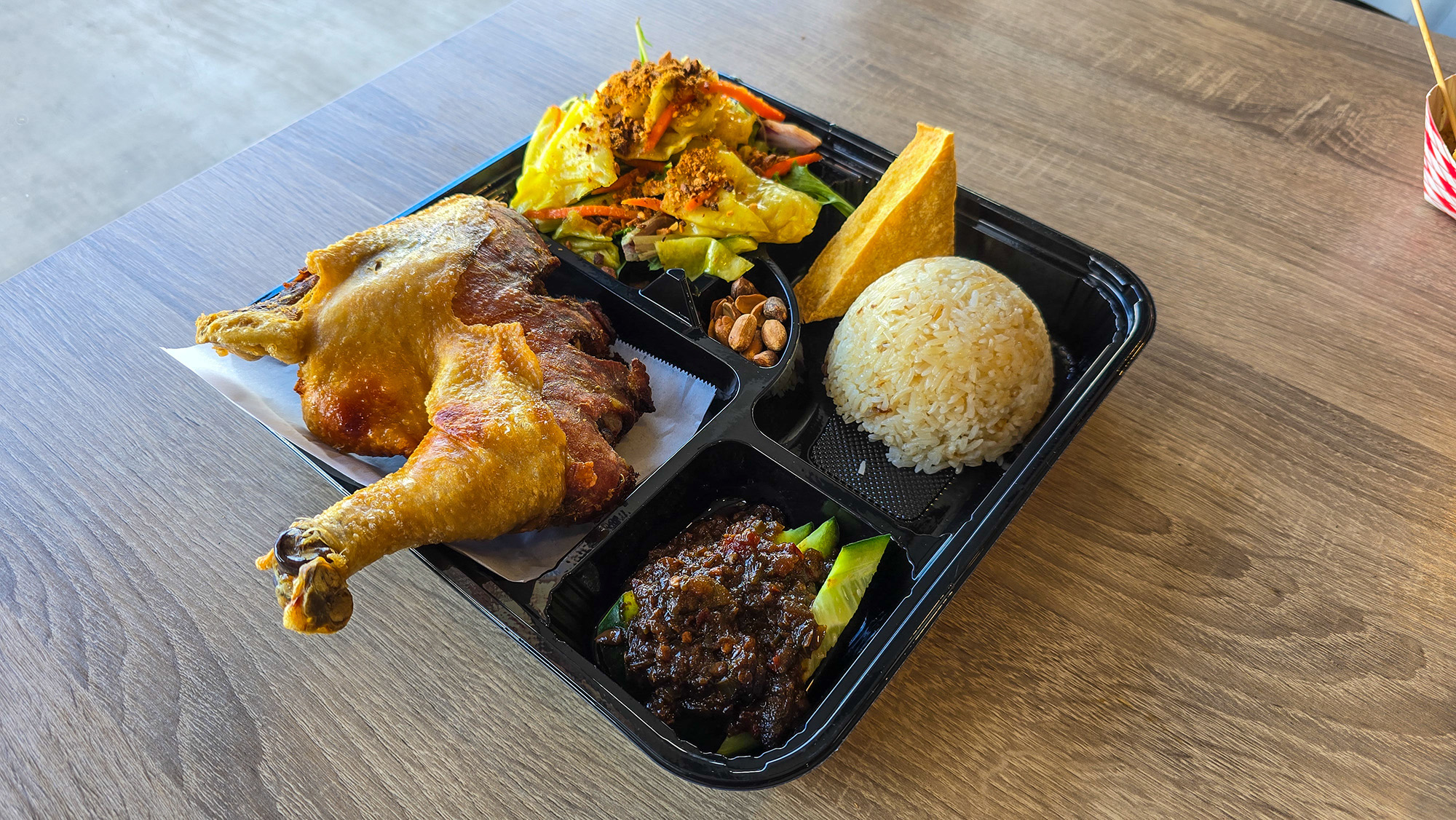 A fried chicken bento box with pickled vegetables, rice and sambal.