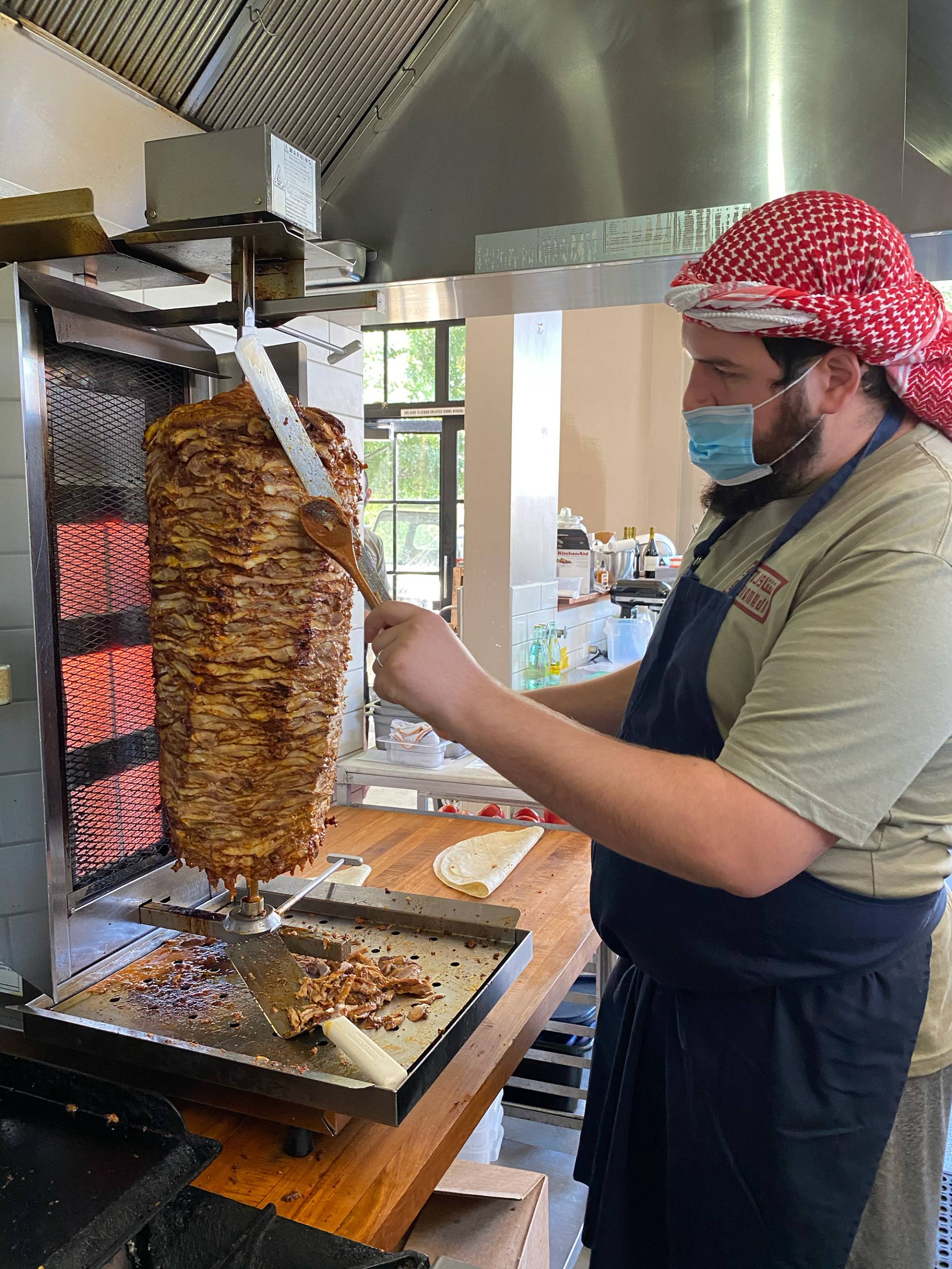 A chef slices meat off of a shawarma spit.
