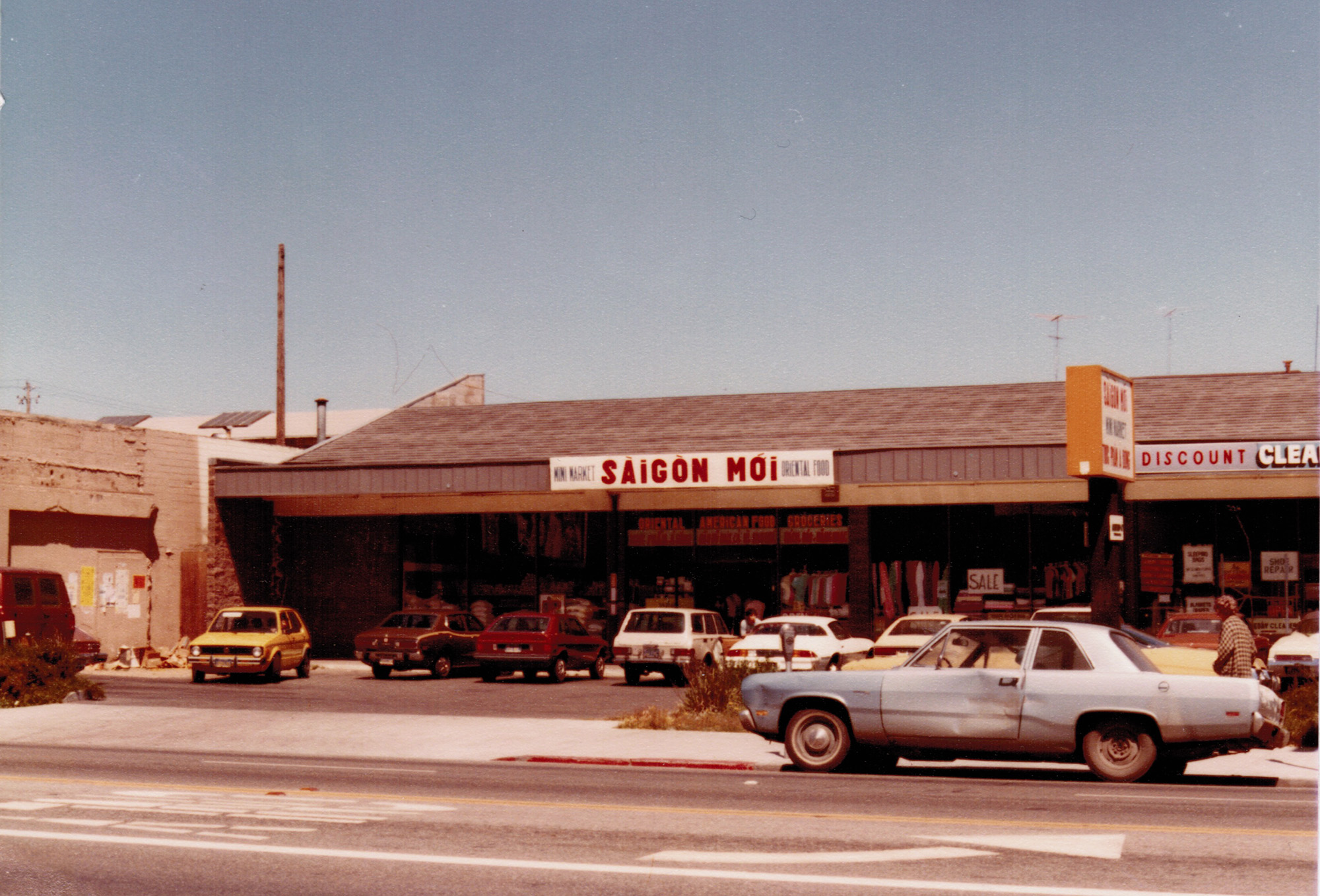 Old 1980s photograph of a Vietnamese grocery store with cars parked outside. The sign reads, 'Sàigòn Mới'. 